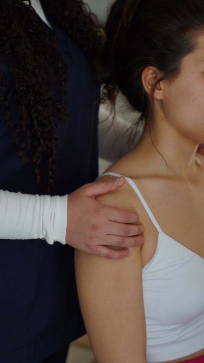 A physiotherapist adjusts a womans shoulder during a therapy session indoors.
